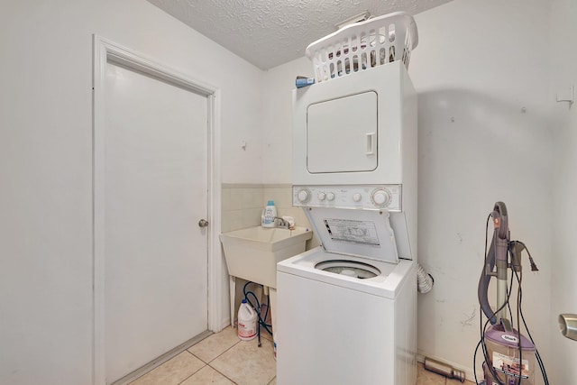 laundry room featuring stacked washing maching and dryer, sink, light tile patterned flooring, and a textured ceiling