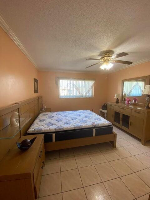 bedroom featuring crown molding, light tile patterned flooring, ceiling fan, and a textured ceiling