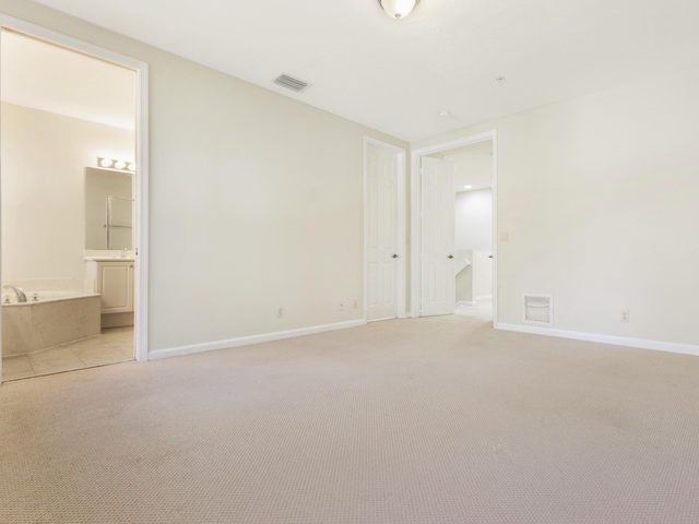 unfurnished bedroom featuring ensuite bathroom and light carpet