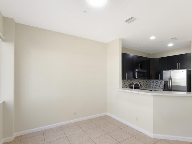 kitchen with sink, light tile patterned floors, appliances with stainless steel finishes, kitchen peninsula, and backsplash