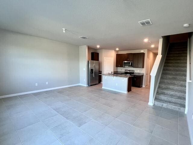 kitchen with stainless steel appliances, an island with sink, and light tile patterned floors