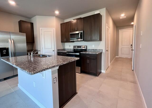 kitchen with sink, a center island with sink, stainless steel appliances, a kitchen bar, and dark stone counters