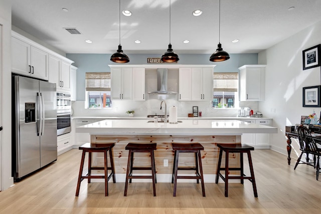 kitchen featuring wall chimney exhaust hood, a breakfast bar, hanging light fixtures, stainless steel appliances, and a kitchen island with sink