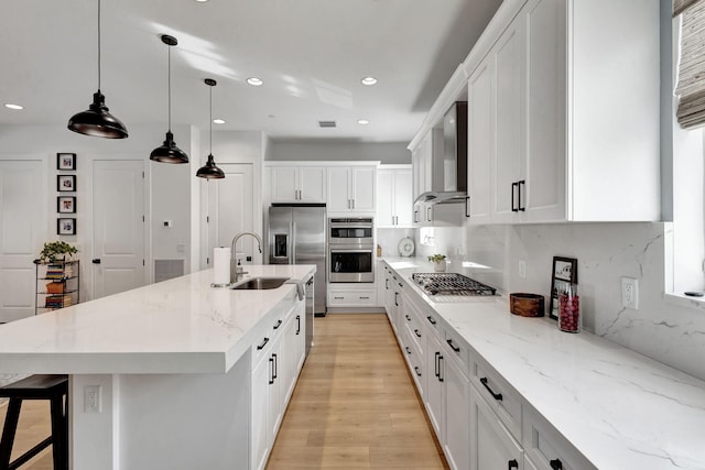 kitchen featuring an island with sink, decorative light fixtures, white cabinets, and wall chimney exhaust hood