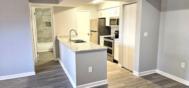 kitchen featuring sink, white cabinetry, light stone counters, appliances with stainless steel finishes, and hardwood / wood-style floors