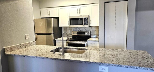 kitchen featuring stainless steel appliances, light stone countertops, decorative backsplash, and white cabinets