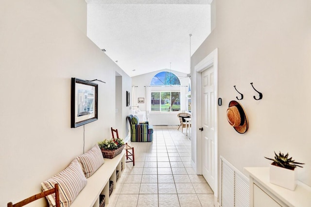 hallway with light tile patterned flooring, vaulted ceiling, and a textured ceiling