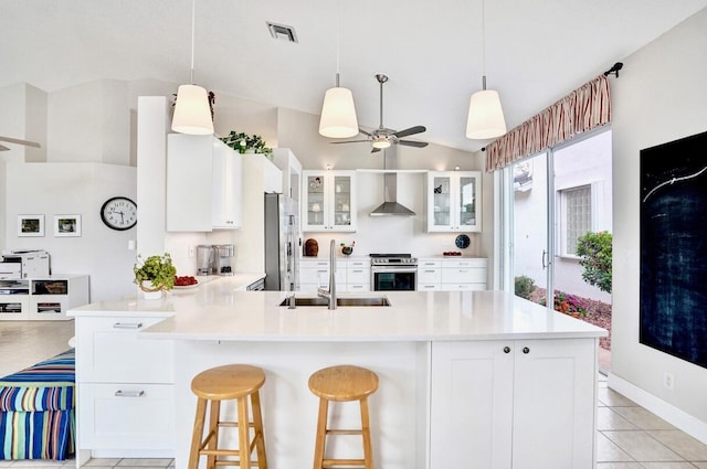 kitchen with appliances with stainless steel finishes, white cabinetry, sink, a breakfast bar area, and wall chimney exhaust hood