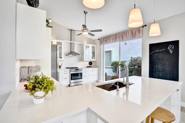 kitchen with a kitchen bar, white cabinetry, kitchen peninsula, stainless steel appliances, and wall chimney range hood