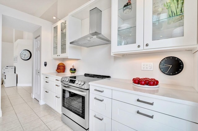 kitchen featuring wall chimney range hood, light tile patterned floors, stainless steel range with electric cooktop, and white cabinets