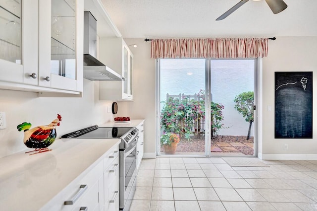 kitchen featuring stainless steel electric range oven, light tile patterned flooring, white cabinetry, ceiling fan, and wall chimney exhaust hood