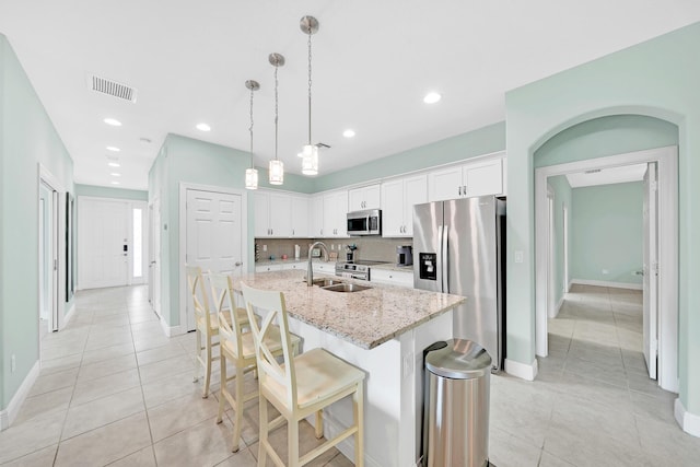 kitchen featuring pendant lighting, white cabinetry, stainless steel appliances, light stone counters, and a center island with sink