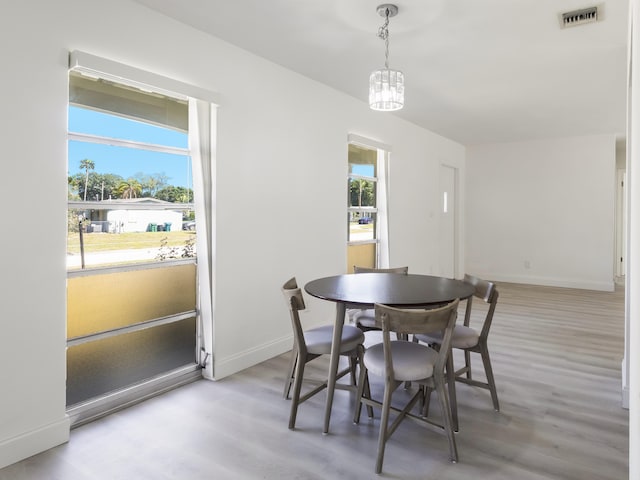 dining space featuring light wood finished floors, baseboards, visible vents, and an inviting chandelier