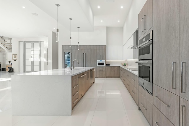 kitchen with appliances with stainless steel finishes, pendant lighting, sink, a large island with sink, and light stone counters