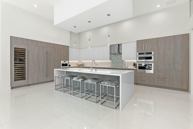 kitchen featuring wall chimney exhaust hood, a breakfast bar, hanging light fixtures, a large island, and a high ceiling