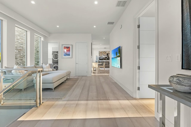 hallway featuring stacked washer / dryer and light hardwood / wood-style flooring