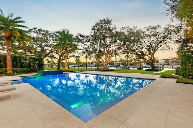 pool at dusk with a patio and a lawn