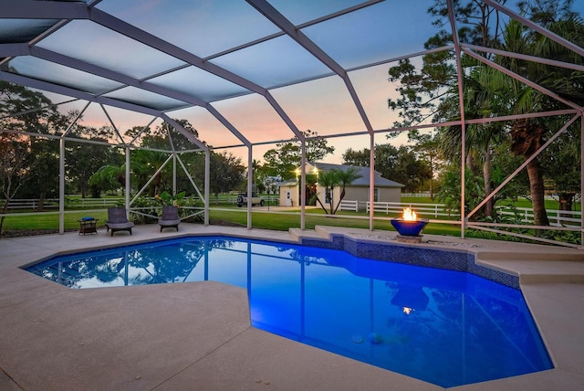 pool at dusk with a patio, a lanai, a lawn, and a fire pit