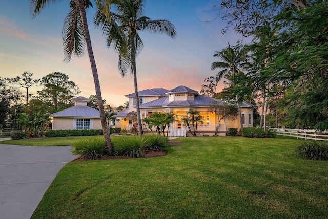 view of front of home with a standing seam roof, fence, metal roof, and a yard