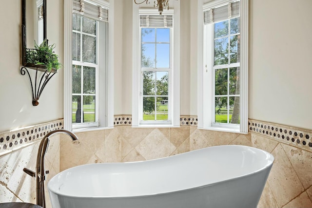 bathroom featuring a wainscoted wall, tile walls, and a freestanding bath