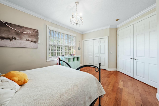 bedroom with crown molding, wood finished floors, baseboards, multiple closets, and an inviting chandelier