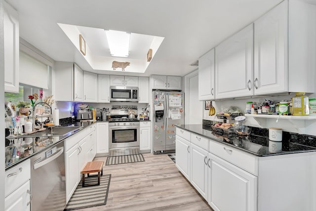 kitchen with white cabinetry, sink, a tray ceiling, stainless steel appliances, and light wood-type flooring