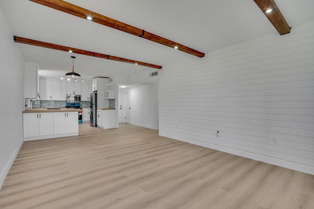 unfurnished living room with baseboards, light wood-style flooring, visible vents, and beamed ceiling