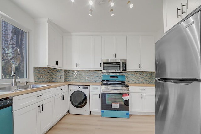 kitchen featuring light wood-style flooring, appliances with stainless steel finishes, white cabinets, a sink, and washer / dryer