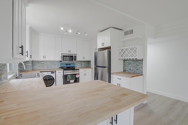 kitchen with open shelves, backsplash, appliances with stainless steel finishes, a sink, and wood counters