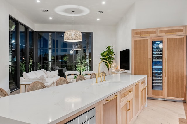 2578 Players Ct, Wellington, FL 33414 - kitchen featuring light brown cabinetry, decorative light fixtures, sink, light stone counters, and light hardwood / wood-style flooring