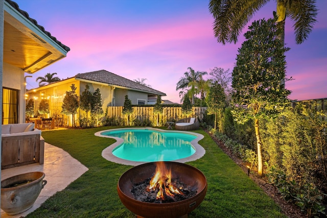 pool at dusk featuring an outdoor fire pit, a patio, and a lawn