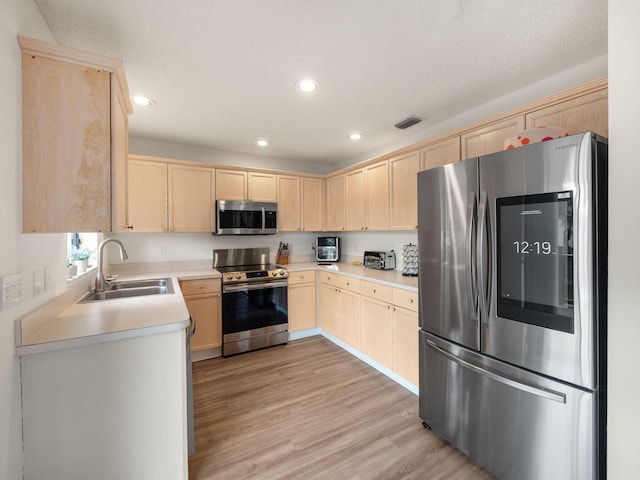 kitchen with light brown cabinetry, sink, light hardwood / wood-style floors, stainless steel appliances, and a textured ceiling