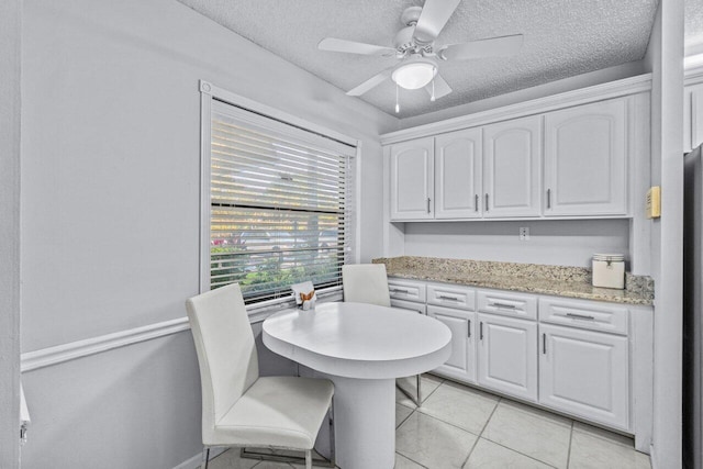 kitchen featuring light tile patterned floors, ceiling fan, light stone countertops, a textured ceiling, and white cabinets