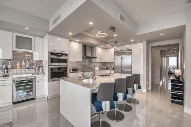 kitchen featuring white cabinetry, wall chimney range hood, stainless steel appliances, and beverage cooler