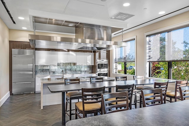 kitchen featuring stainless steel appliances, dark parquet floors, white cabinets, a center island with sink, and decorative backsplash