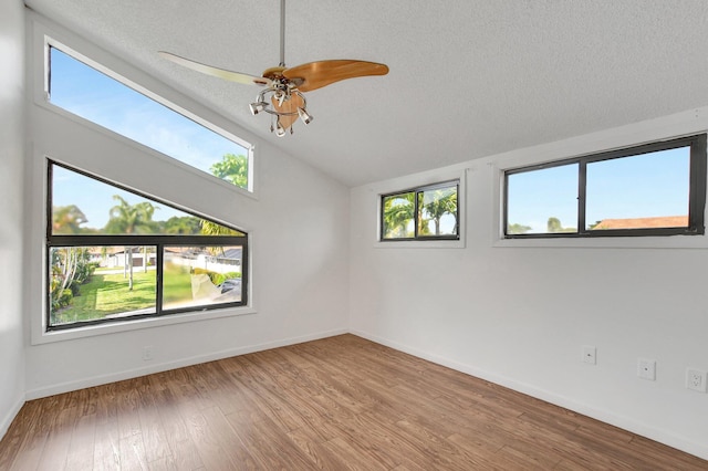 spare room with a textured ceiling, baseboards, wood finished floors, and lofted ceiling