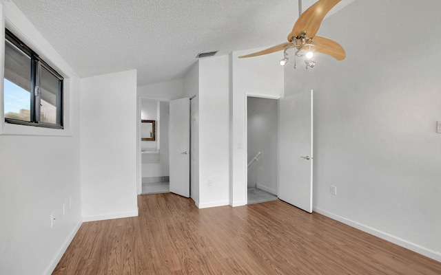 unfurnished bedroom featuring lofted ceiling, visible vents, a textured ceiling, and wood finished floors