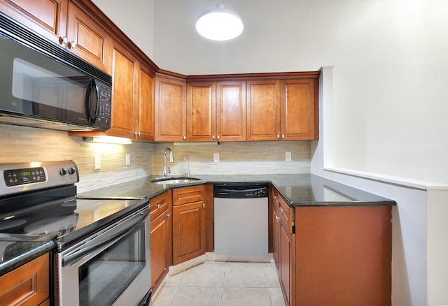 kitchen featuring stainless steel appliances, brown cabinetry, dark stone countertops, and a sink