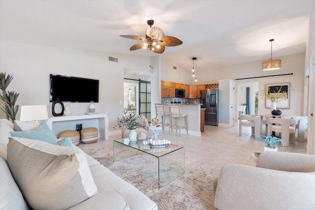 living room with ceiling fan, a barn door, vaulted ceiling, and light tile patterned floors