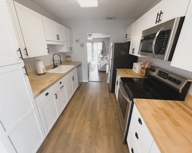 kitchen featuring appliances with stainless steel finishes, sink, white cabinetry, and butcher block counters