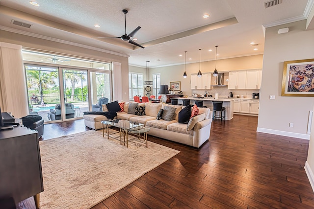 living room with dark hardwood / wood-style flooring, ornamental molding, a raised ceiling, and ceiling fan