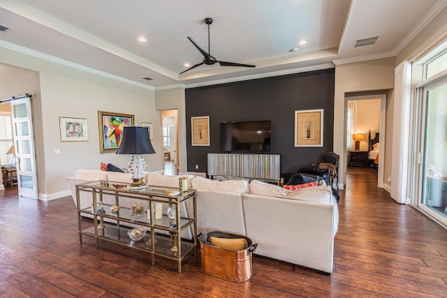 living room featuring a healthy amount of sunlight, dark hardwood / wood-style floors, a barn door, and a raised ceiling