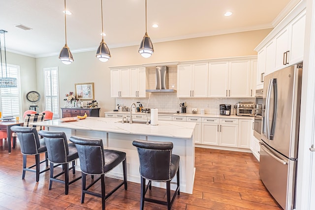 kitchen with pendant lighting, wall chimney range hood, white cabinetry, and stainless steel appliances