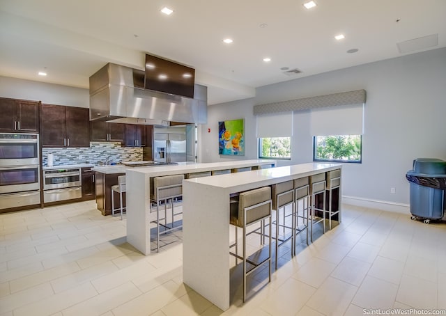 kitchen with island exhaust hood, a kitchen island, a kitchen breakfast bar, and appliances with stainless steel finishes