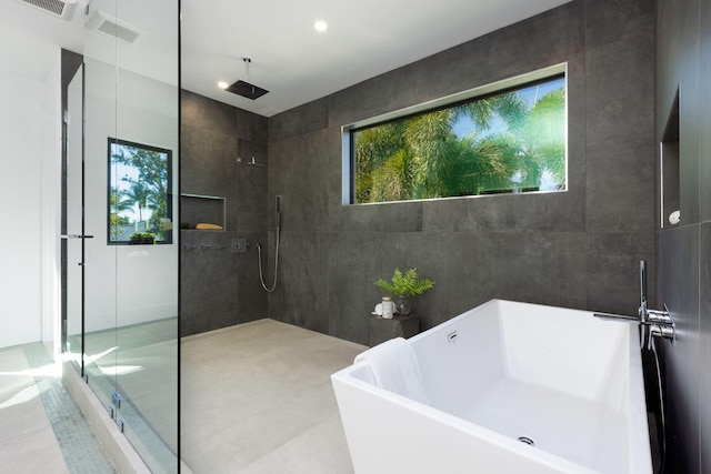 bathroom with plus walk in shower, a healthy amount of sunlight, and tile walls