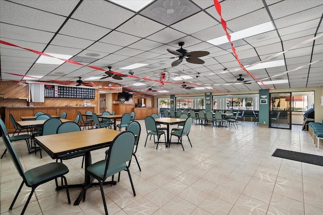 dining space featuring a drop ceiling, ceiling fan, and wood walls