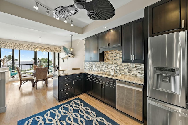 kitchen with appliances with stainless steel finishes, decorative light fixtures, sink, light stone counters, and kitchen peninsula