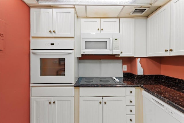 kitchen featuring white cabinetry, dark stone countertops, and white appliances