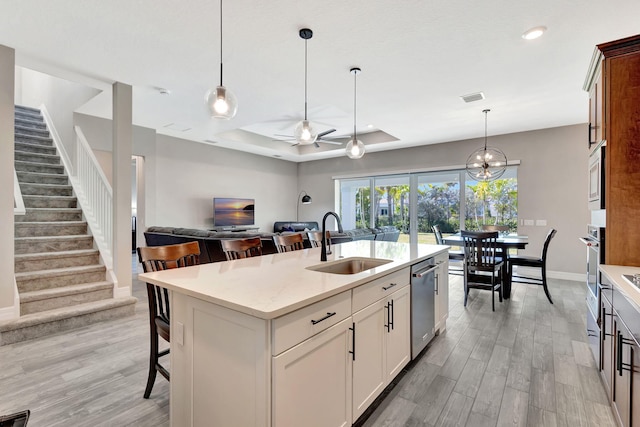 kitchen featuring a breakfast bar, an island with sink, sink, hanging light fixtures, and light stone counters