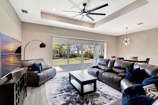 living room featuring ceiling fan with notable chandelier, a tray ceiling, and light hardwood / wood-style floors